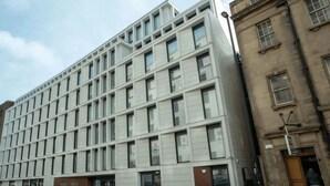 Un edificio moderno con una fachada de ventanas en forma de cuadrícula y una entrada marrón con la leyenda 