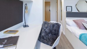 Un dormitorio moderno con escritorio, una silla, una cama y un estante con una planta.