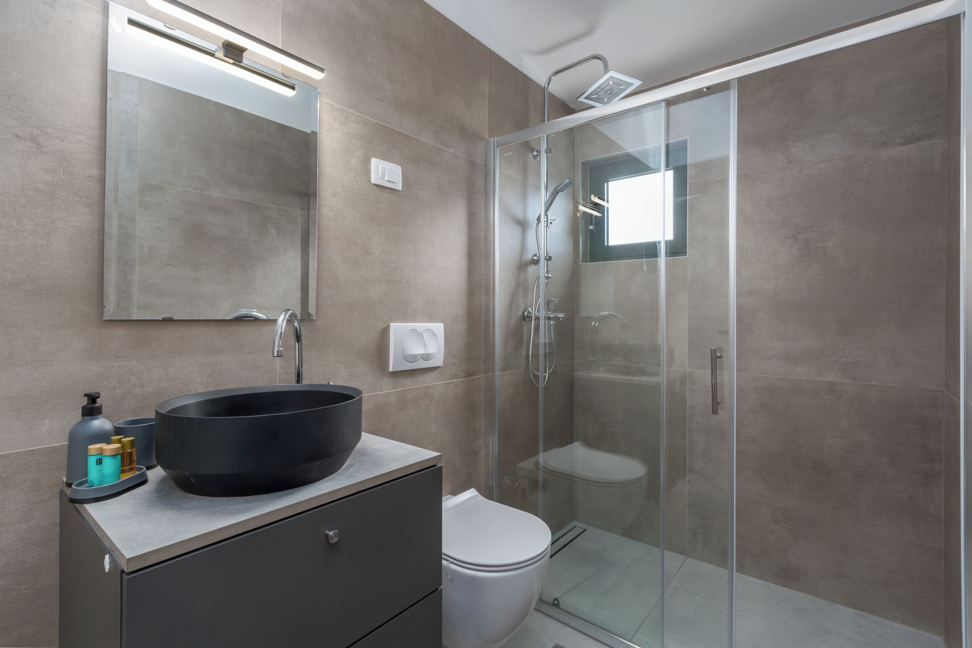 A modern bathroom with a large black sink, a toilet, and a glass-enclosed shower area.