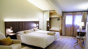 Et hotelværelse med en stor seng, et træhovedgærde, et sengebord med en lampe, en stol og et lille skrivebord med lampe.