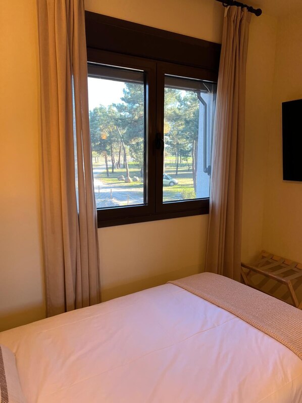 A bedroom with a bed, a window with curtains, and a view of trees and a car outside.