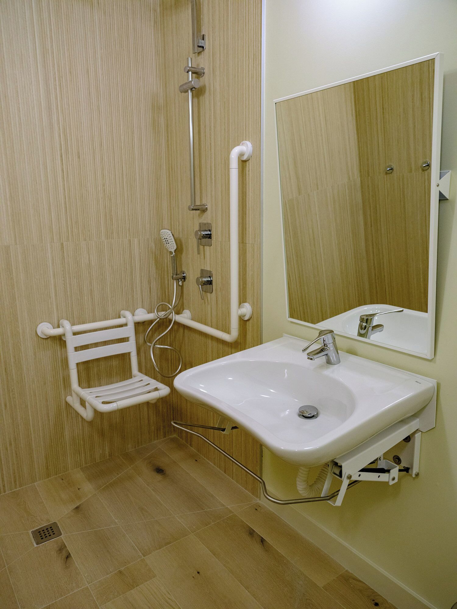 A bathroom with a wooden floor, a white sink with a mirror above it, and a shower area with a white grab bar.