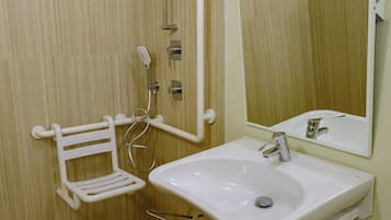 A bathroom with a wooden floor, a white sink with a mirror above it, and a shower area with a white grab bar.