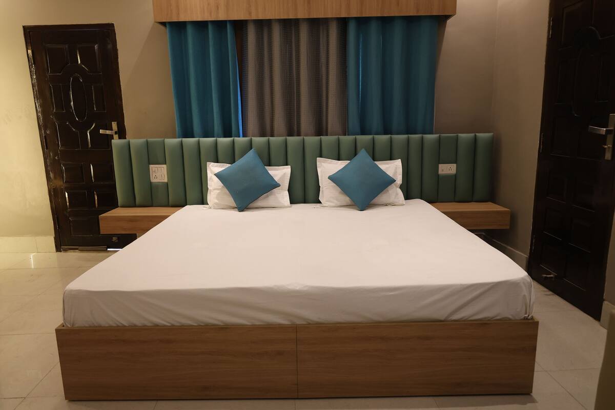 A hotel room with a large bed, a wooden headboard, and a view of the outside through a window with curtains.