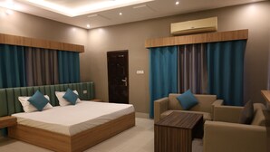 A modern hotel room with a large bed, a sofa, a small table, and a door. - River View Resort (Haridwar)