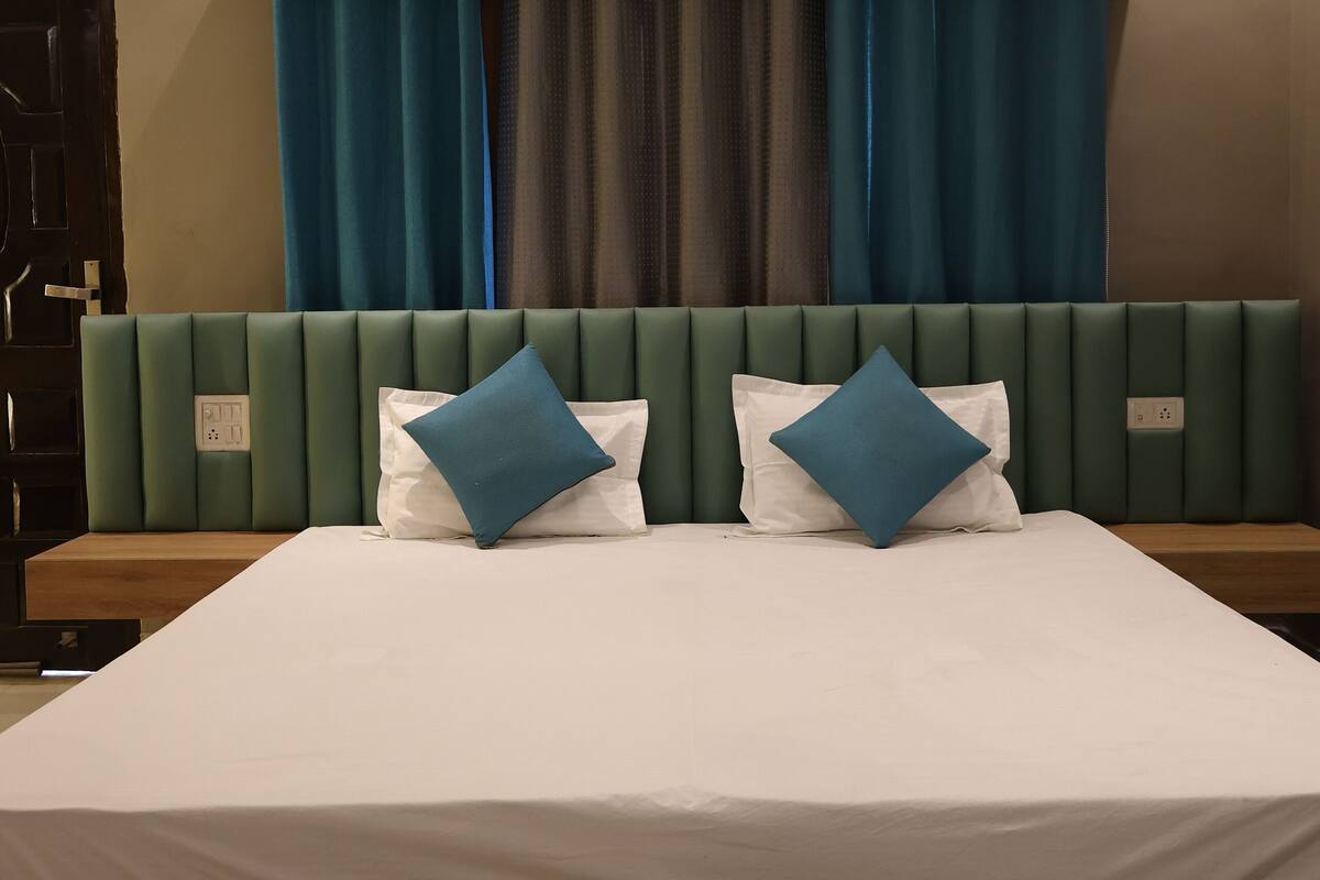 A modern hotel room with a large bed, green upholstered headboard, and blue curtains.