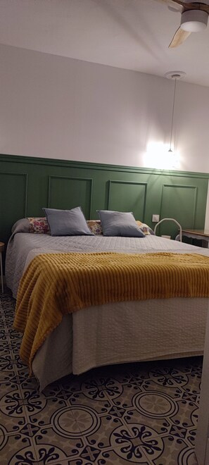 Een bed met een bedspread met dessin en kussens, een groen hoofdbord en een vloer met patroon.