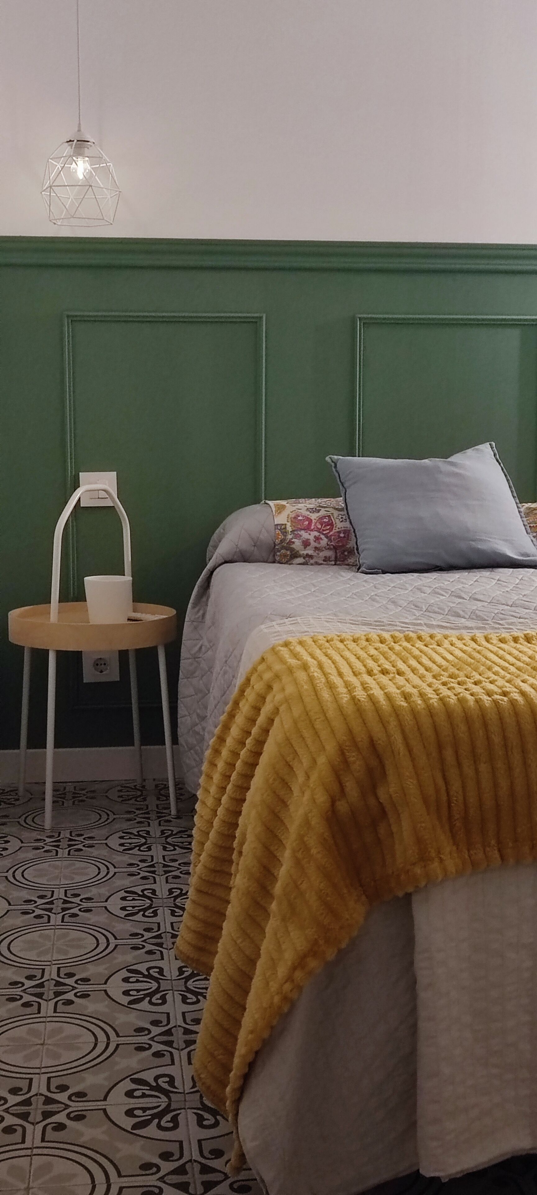 Una habitación con cama, una silla, lámpara colgante y piso estampado.