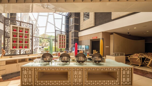 A modern hotel lobby with a central island featuring a grill station, surrounded by seating and a glass partition with red decorative items. - Dancenter Promenade Near Cihampelas Walk (Bandung)