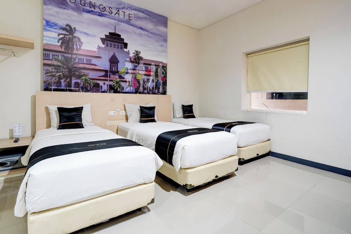 Ein Hotelzimmer mit drei Betten, einem großen Poster an der Wand und einem Fenster mit Jalousie.