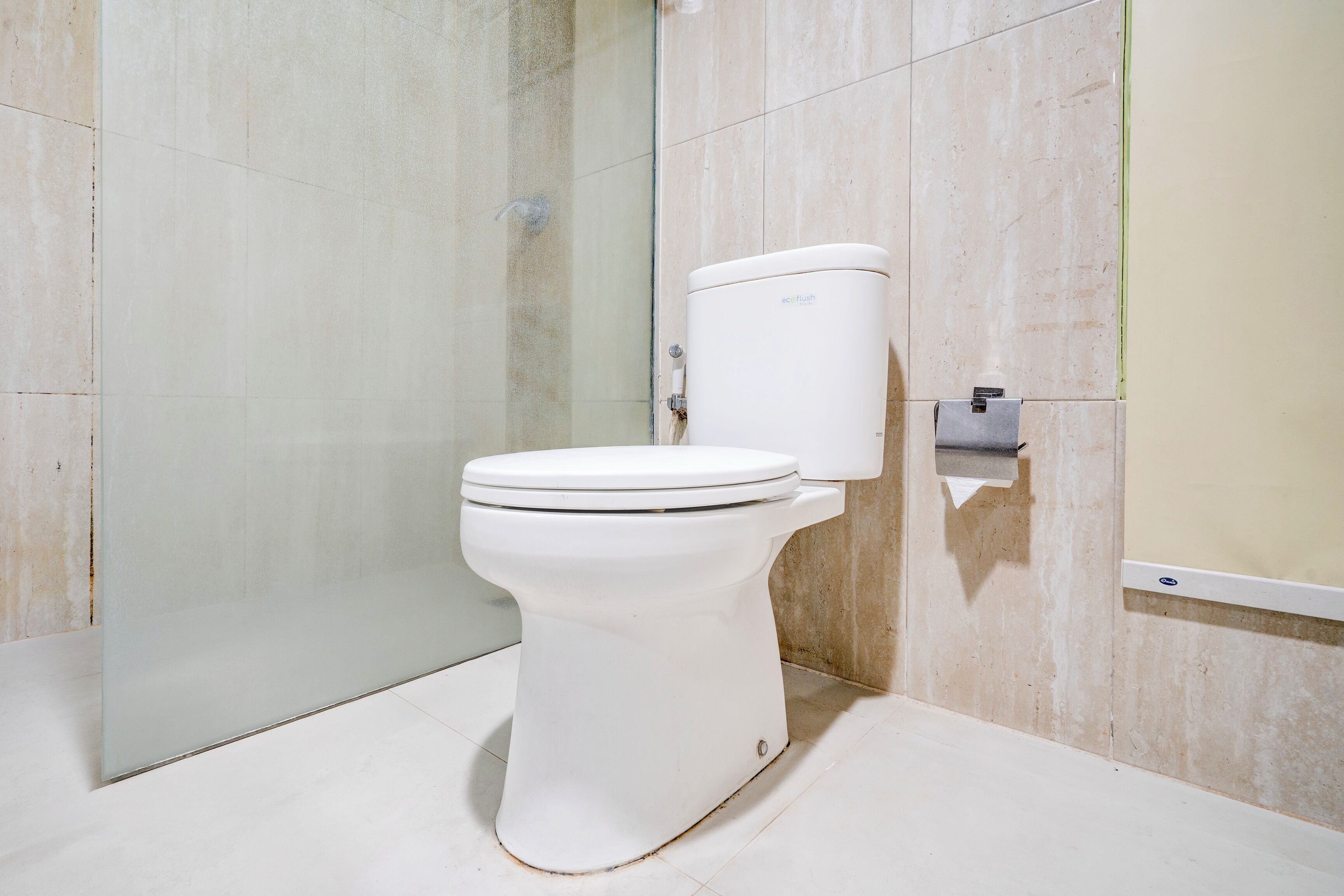 A modern bathroom with a white toilet, a glass shower enclosure, and a marble-tiled wall.
