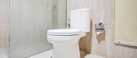 A modern bathroom with a white toilet, a glass shower enclosure, and a marble-tiled wall.