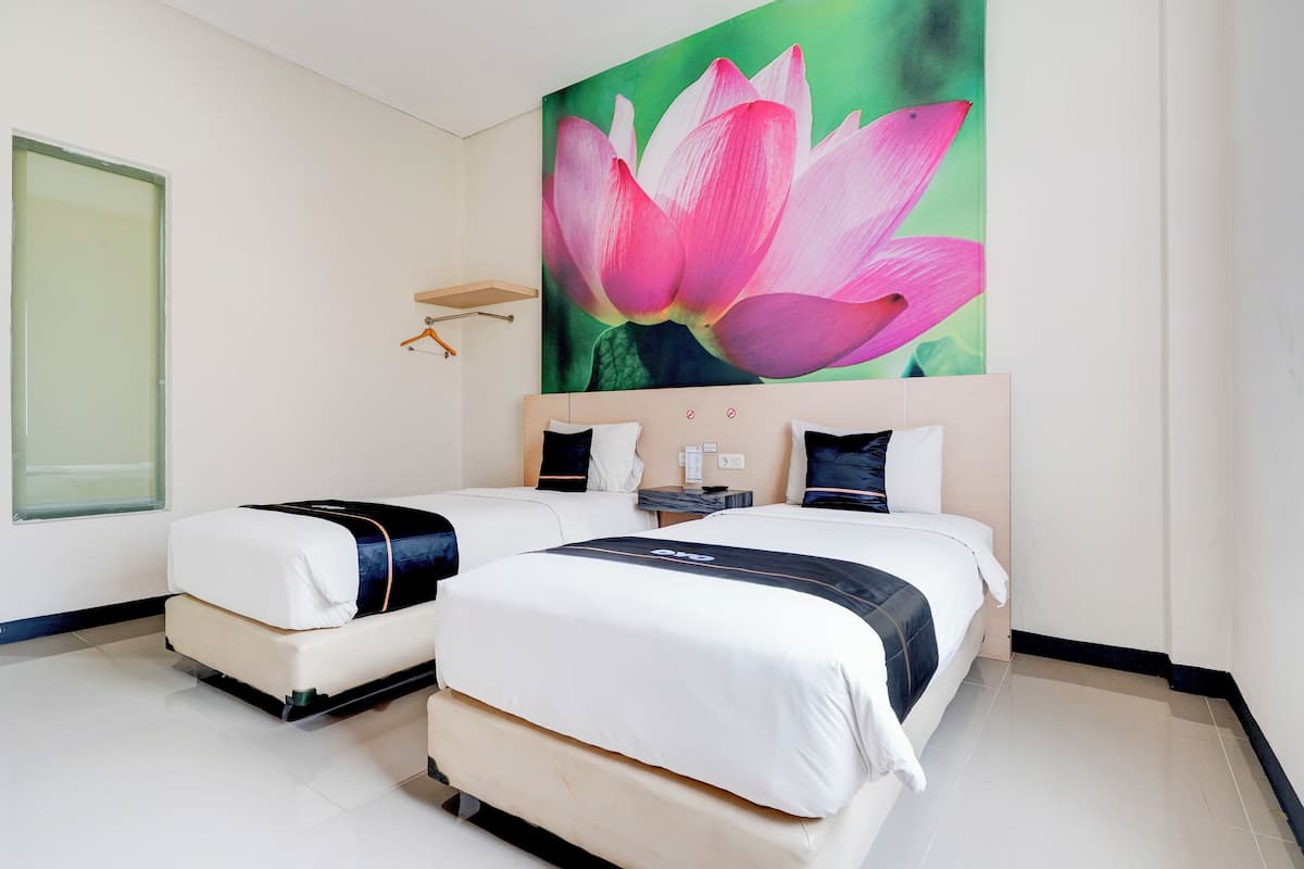 Ein Hotelzimmer mit zwei Betten, einem großen Wandbild einer rosa Blume und einem kleinen Tisch mit einer Lampe.