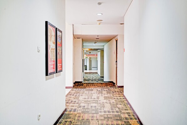 Un couloir d’hôtel avec des tableaux encadrés accrochés aux murs, un revêtement de sol en moquette et un panneau de signalisation indiquant la sortie.
