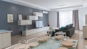 En moderne stue med spiseplads, der indeholder en sofa, et fjernsyn og et spisebord med tallerkener og glas.