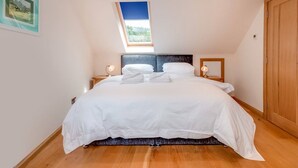 A bedroom with a skylight, a bed with white bedding, two bedside tables with lamps, and a wooden wardrobe.