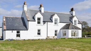 A white two-story house with a grey roof, multiple chimneys, and a stone wall foundation.
