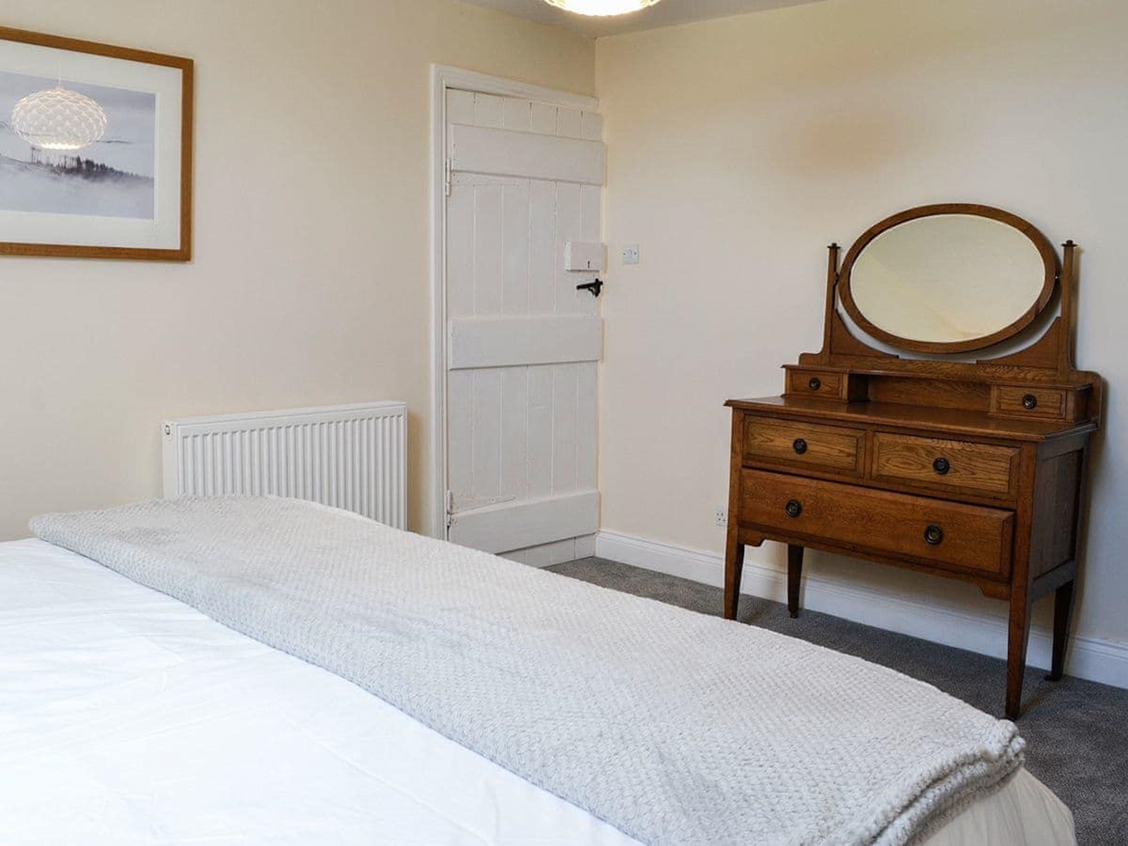 A bedroom with a bed, a wooden dresser with a mirror, a white door, and a framed picture on the wall.