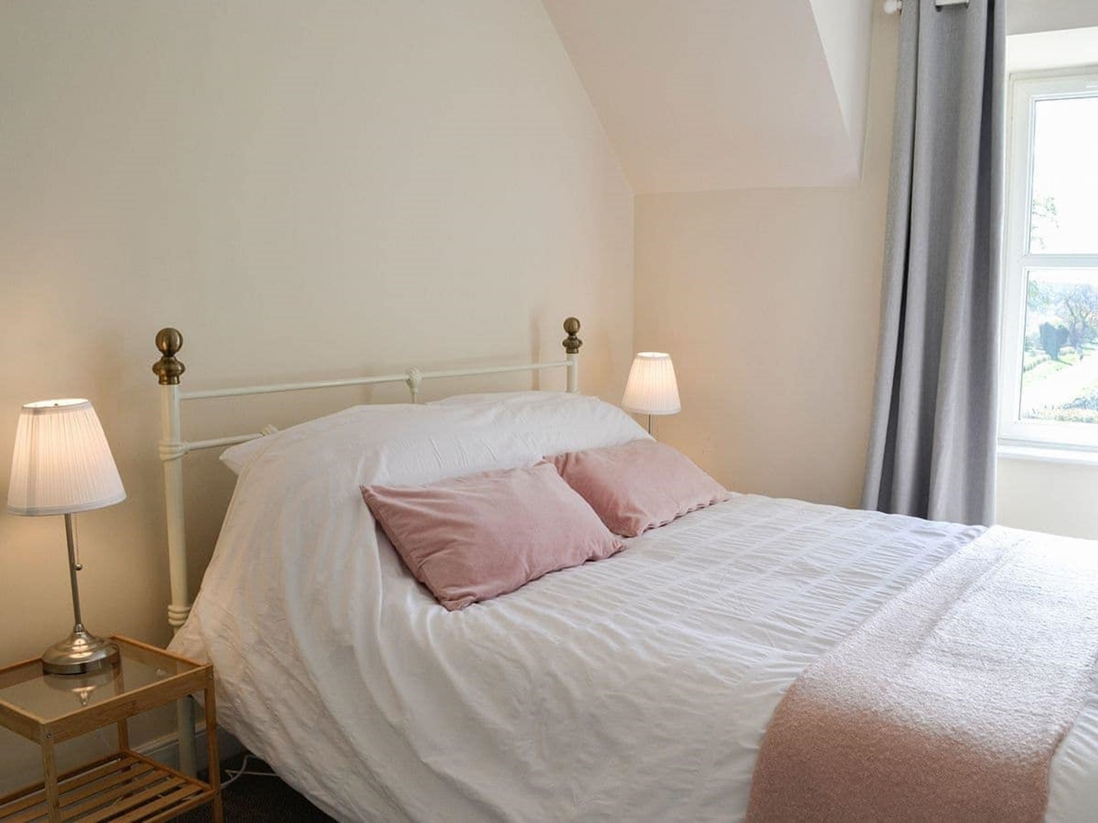 A bedroom with a bed, two bedside tables, and a window with curtains.
