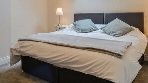 A neatly made bed with a grey headboard, a bedside lamp, and a skylight above.