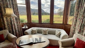 A room with a red carpet, a round table, and two sofas with red cushions. - Sherramore Lodge -  a lodge that sleeps 19 guests  in 10 bedrooms (Laggan)