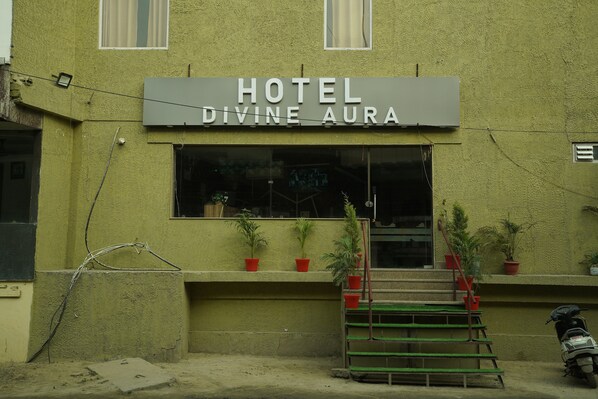 A building with a sign reading "HOTEL DIVINE AURA." There are steps leading up to the entrance, and several potted plants are placed on the steps and on the ground.