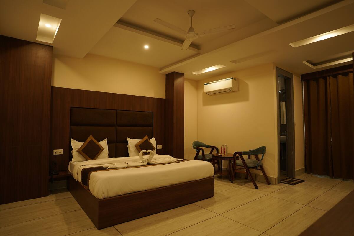 A hotel room with a large bed, a ceiling fan, an air conditioning unit, and two chairs.