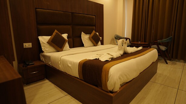 A hotel room with a large bed, a wooden headboard, a bedside table with a lamp, and a chair.