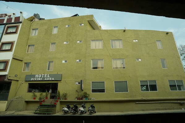 A multi-story building with a sign reading "HOTEL DIVINE AURA." There are several windows, some with curtains, and a few potted plants on the ground floor. - Hotel Divine Aura - A Premium Hotel (Haridwar)