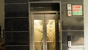 An elevator with a glass door, a fire emergency button, and a sign instructing to use the stairs in case of fire.