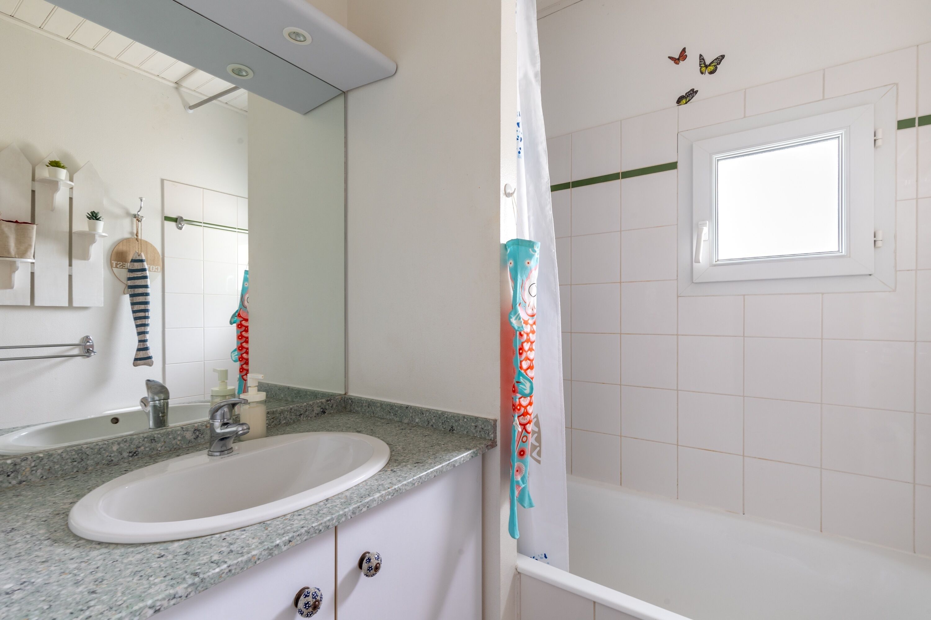 A bathroom with a white sink, a mirror, a shower curtain, and a window.