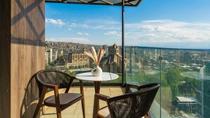 Un balcon doté d’une balustrade en verre, d’une table ronde et de deux chaises en osier.