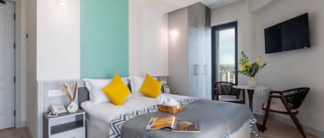 A modern hotel room with a bed, bedside table, nightstand, and a small seating area with a chair and table.