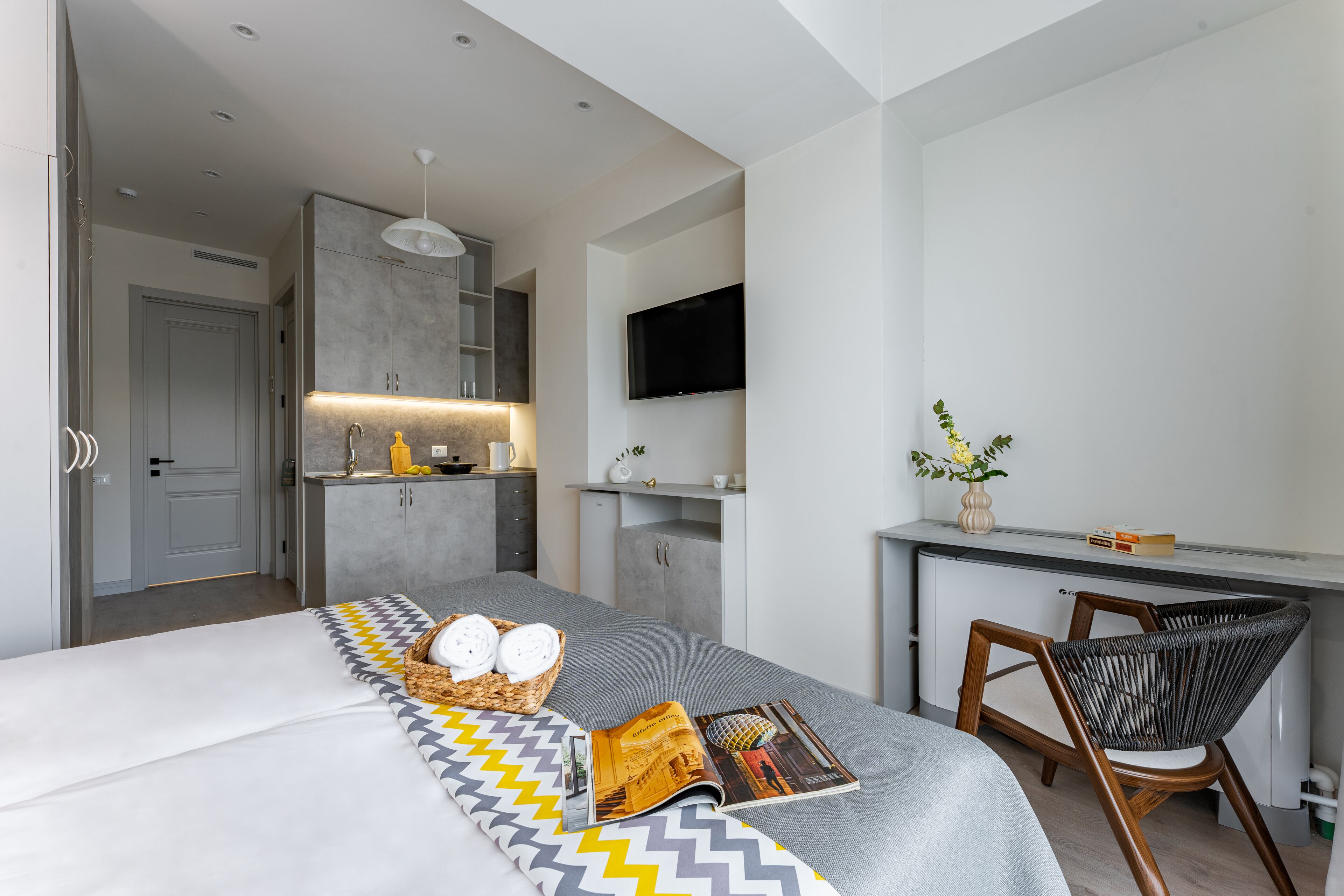 A modern hotel room with a bed, a desk, a chair, and a TV.