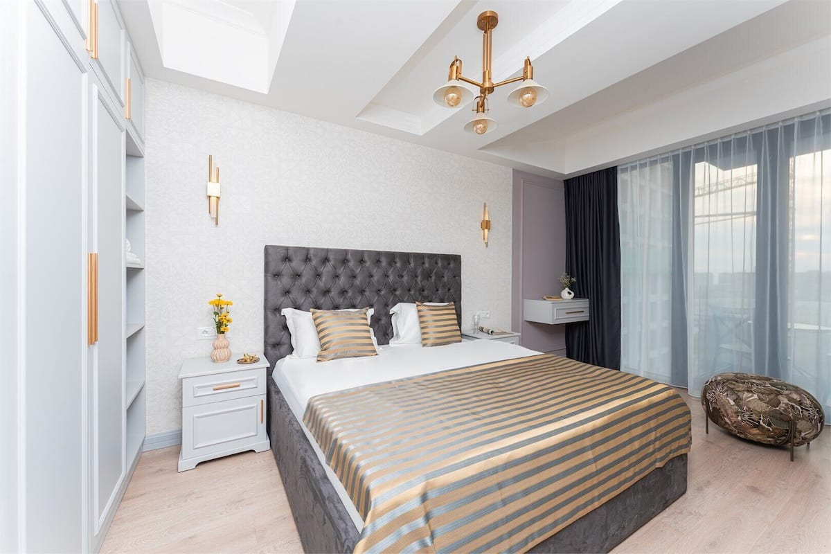 Habitación de hotel moderna con una cama grande, una mesita de noche, un adorno de pared y vistas a la ciudad por la ventana.