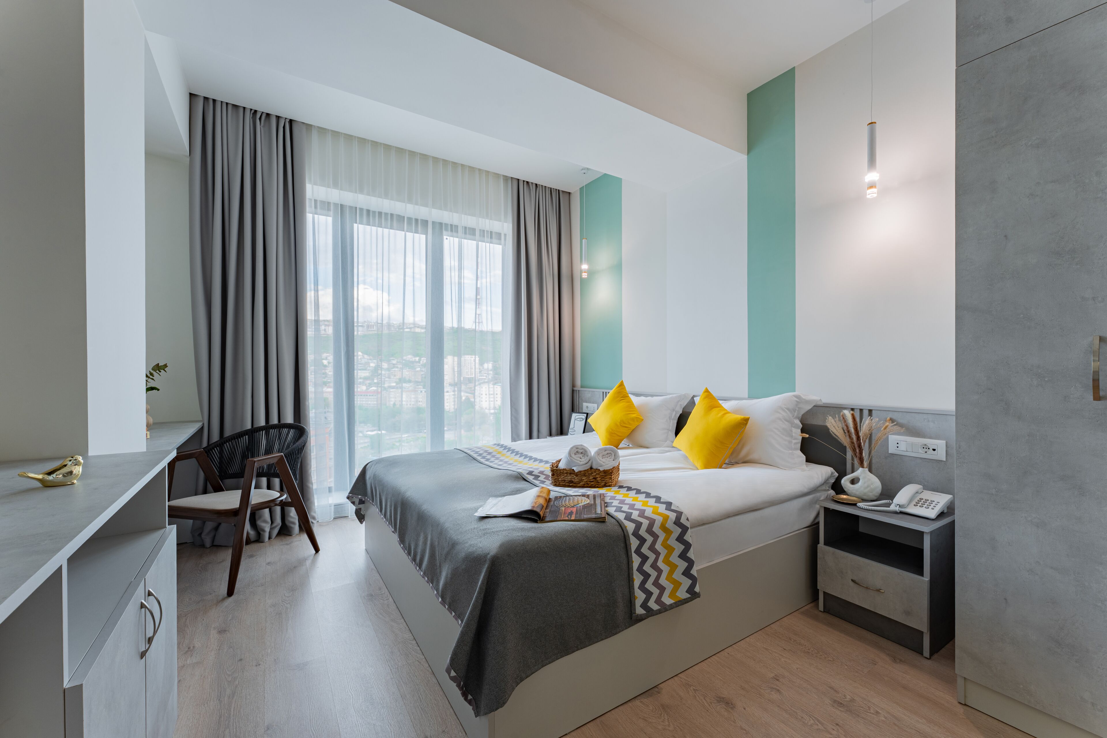 A modern hotel room with a large bed, a desk, a chair, and a view of the city.