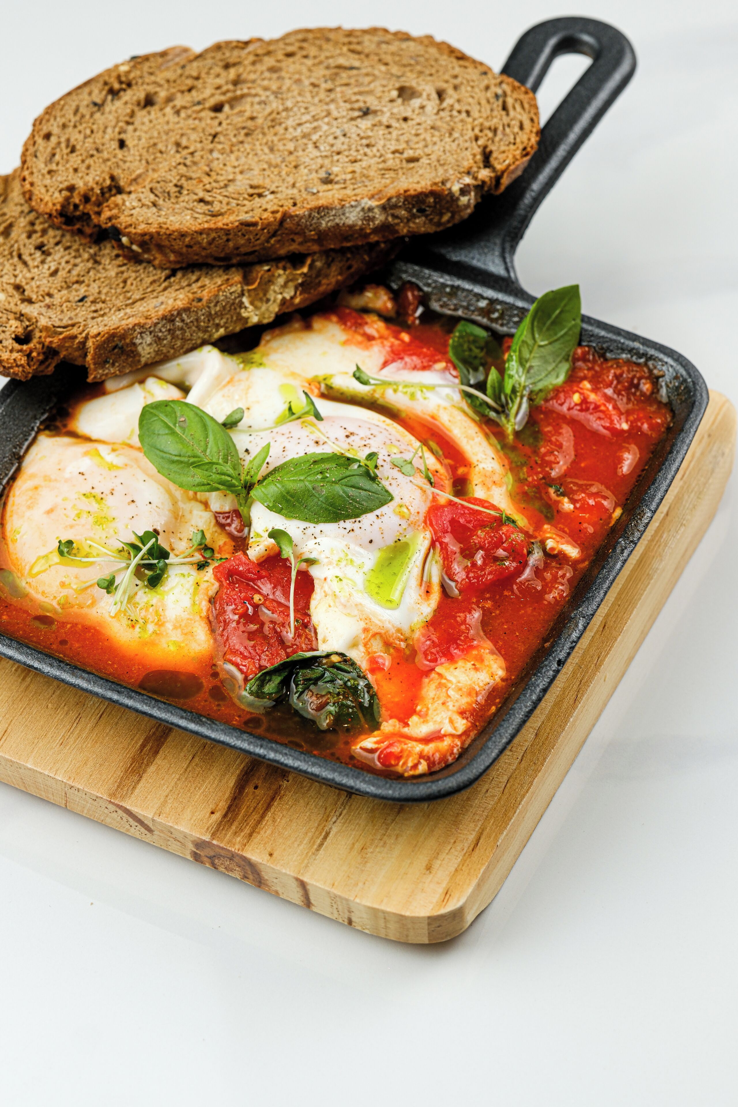 A skillet with eggs and tomatoes, accompanied by slices of bread on a wooden board.