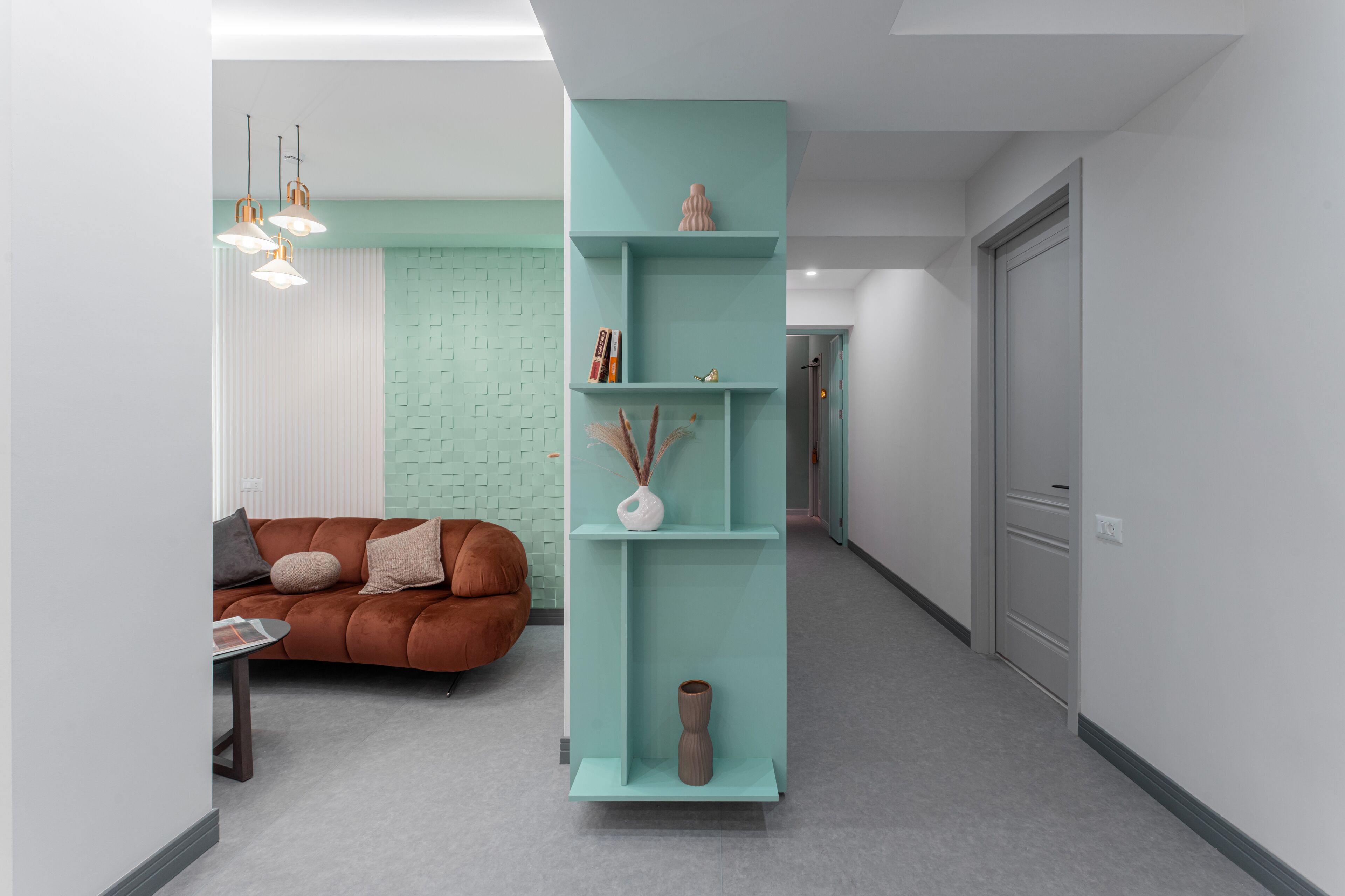 En moderne stue med en teal farvet væg, en brun sofa og et højt reolsystem med dekorative genstande.