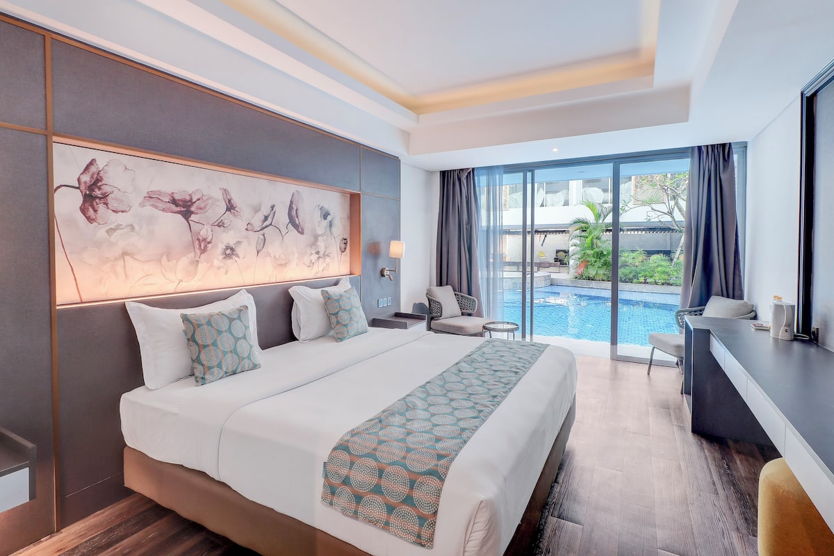 Una camera d'albergo moderna con un letto grande, una scrivania e vista su una piscina.