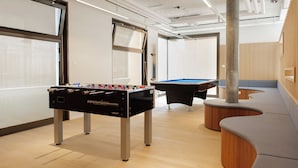 A modern indoor recreational area with a foosball table, pool table, and seating area. - Geneva Youth Hostel (Vernier)