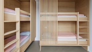 A bunk bed with a wooden slat divider, multiple shelves, and a concrete floor. - Geneva Youth Hostel (Vernier)