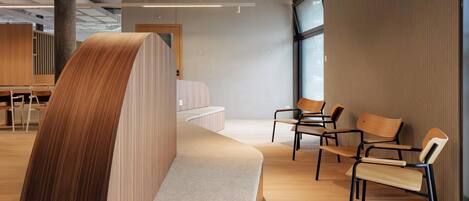 A modern interior with a curved bench, wooden chairs, and a large window.