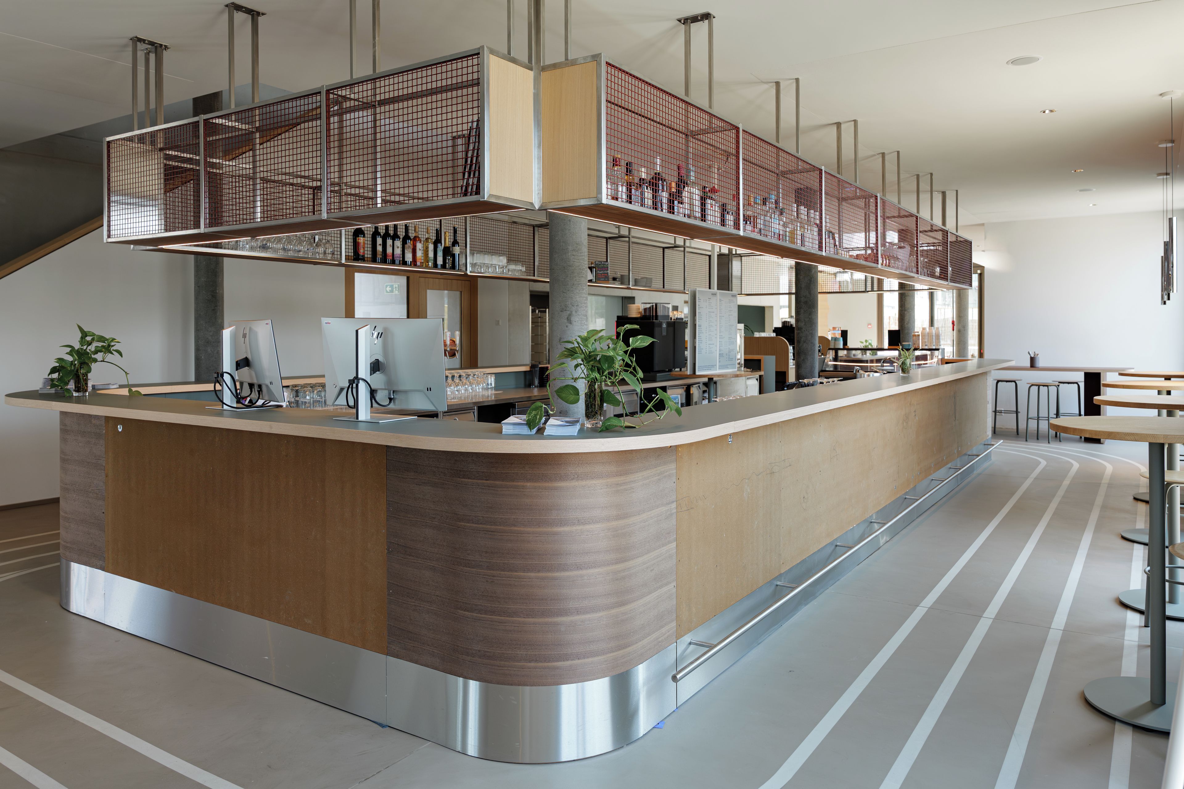 A modern bar area with a curved counter, metal mesh railings, and a variety of bottles and glasses.