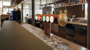 A bar area with a long counter, multiple beer taps, and a selection of bottles on the shelf. - Geneva Youth Hostel (Vernier)