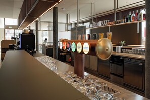 A bar area with a long counter, multiple beer taps, and a selection of bottles on the shelf. - Geneva Youth Hostel (Vernier)