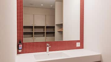 Un baño con un lavamanos blanco, paredes de baldosas rojas y un espejo que refleja un armario y estanterías.
