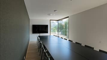 Un salón de conferencias con una larga mesa, sillas, un televisor de pantalla plana y ventanas amplias.