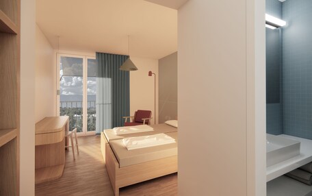 A modern hotel room with a wooden desk, two beds, a red chair, a large window with a view, and a bathroom with a blue tiled wall.
