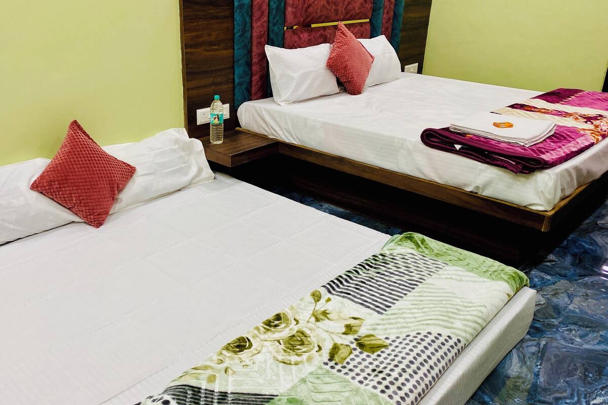 Two single beds with white linens and red pillows, a water bottle on the nightstand, and a patterned bedspread on the right bed.