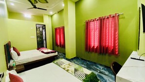 A room with a bed, a desk, and a window with red curtains. - Hotel Shree Sita Ram Kutti (Ujjain)